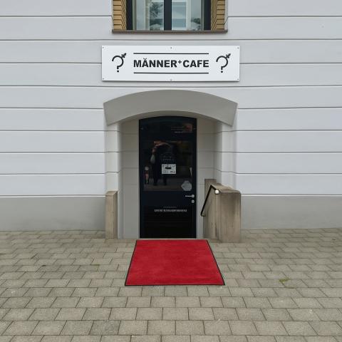 Eingang zumMÄNNERCAFE mit rotem Teppich